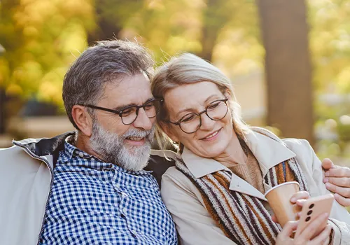 Reifes Pärchen sitzt auf einer Bank in der Natur und informiert sich über die Finanzierung ihrer Photovoltaikanlage.