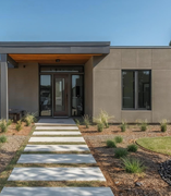 Modernes, ebenerdiges Einfamilienhaus mit Flachdach, grauer Fassade, großer Garage und minimalistisch gestalteter Gartenanlage