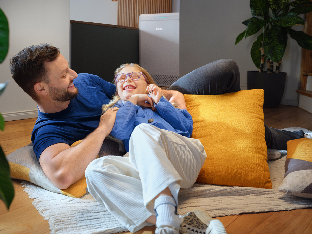 Vater und Tochter lachen gemeinsam auf dem Wohnzimmerboden – gemütliches Zuhause mit nachhaltiger Energie durch Photovoltaik