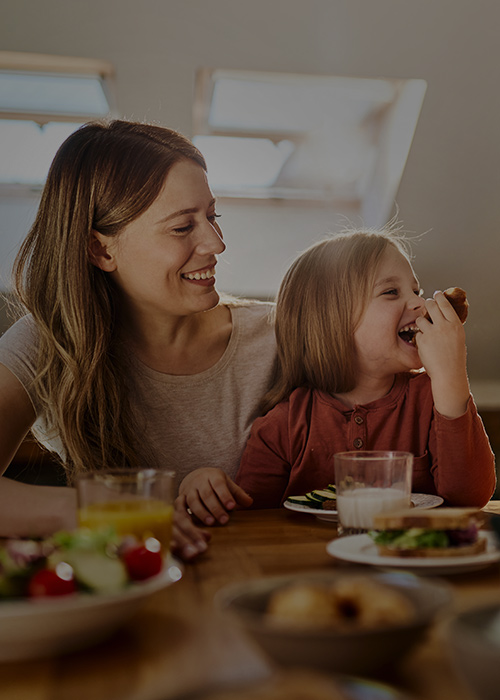 Lächelnde Familie mit zwei kleinen Kindern sitzt gemeinsam am Esstisch unter dem Dach und genießt eine Mahlzeit.